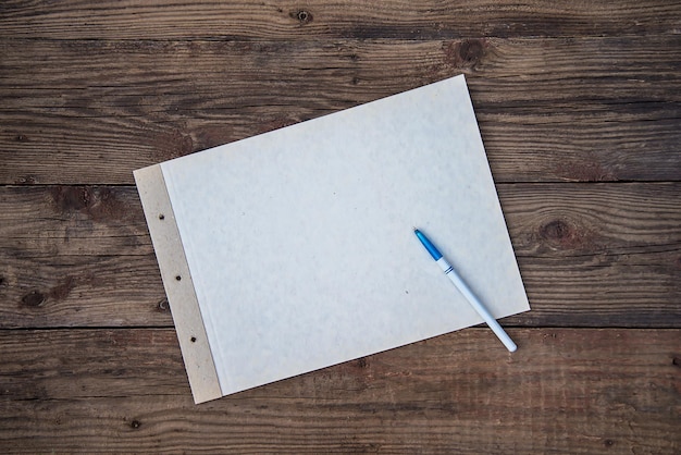 Ein Blatt schweres weißes Papier mit Stift auf einem rauen Holzhintergrund mit Kopierraum