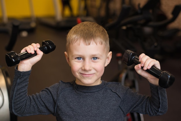 Ein blauäugiger Junge trainiert mit Hanteln in einem Rehabilitationszentrum oder Fitnessstudio