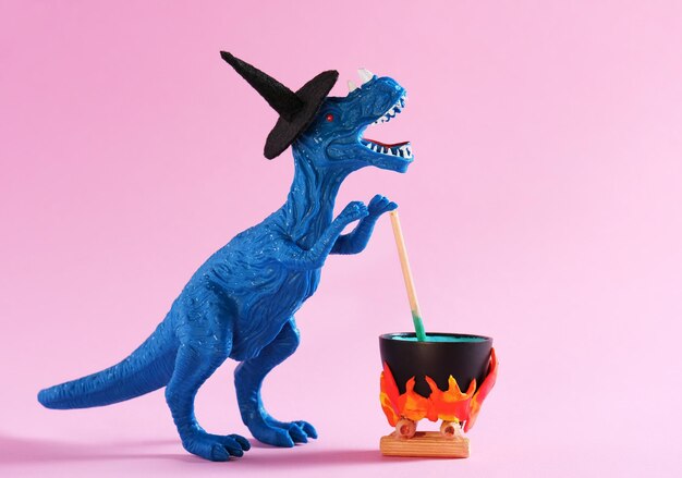 Ein blauer Dinosaurier, der einen Hexenhut trägt, braut einen Trick in einem Topf auf einem pinkfarbenen Hintergrund.