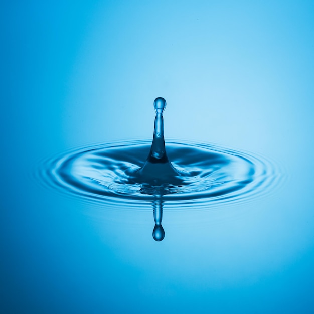 Ein blauer trinkwasser tropfen über der wasseroberfläsche. Erstellt im Studio mit einer 5D mark III.