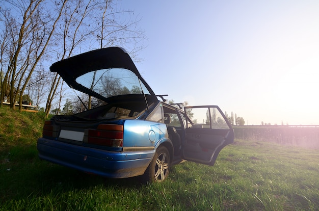 Ein blaues Auto auf einem Hintergrund einer rustikalen Landschaft mit einem wilden Stockfeld und einem kleinen See. Die Familie kam in der Nähe des Sees zur Ruhe