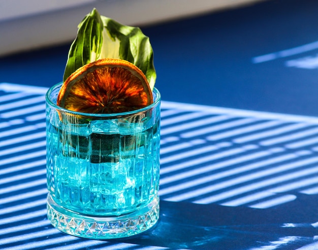 Ein blaues Cocktailglas mit einem Stück Orange auf einem blauen Tisch mit blauen Schatten Platz kopieren