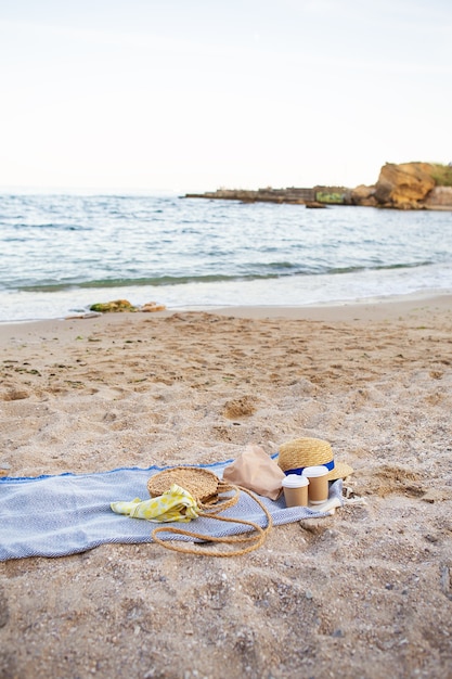 Ein blaues Plaid, auf dem Plastikgläser mit Kaffee stehen, eine Tasche, ein Hut am Meer.