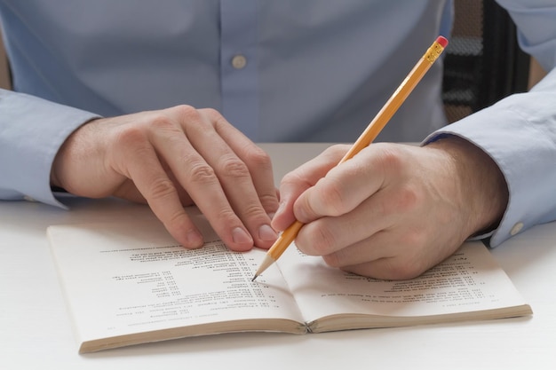 Ein Bleistift in der Hand eines Mannes macht Markierungen in einem Buch