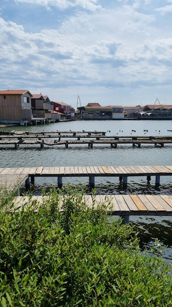 Ein Blick auf das Wasser mit einem Holzsteg im Vordergrund und einem Gebäude im Hintergrund.