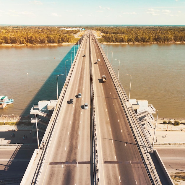 Ein Blick auf die Stadtbrücke und den Flussdamm. Eine gerade Linie einer gut ausgebauten Autobahn über das Flussufer. Stadtverkehr über den Fluss. Autos, die über eine Flussbrücke fahren. Banken überbrücken.