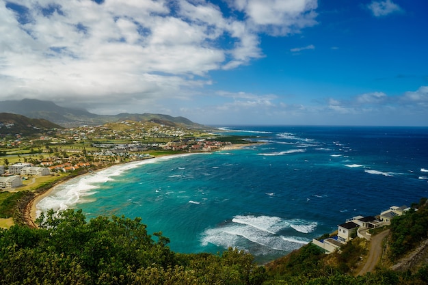 Ein Blick über St. Kitts Island mit Wohngebiet und Strand im Vordergrund und üppig grünen Hügeln