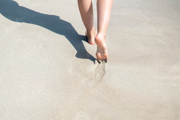 Ein Blick von hinten auf eine Person, die mit nackten Füßen am Sandstrand spaziert