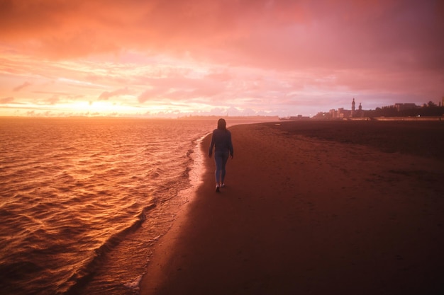 Foto ein blick von hinten ein mädchen geht allein am stadtstrand spazieren und blickt auf den farbenfrohen sonnenuntergang nach dem regen orange purpurrote farben