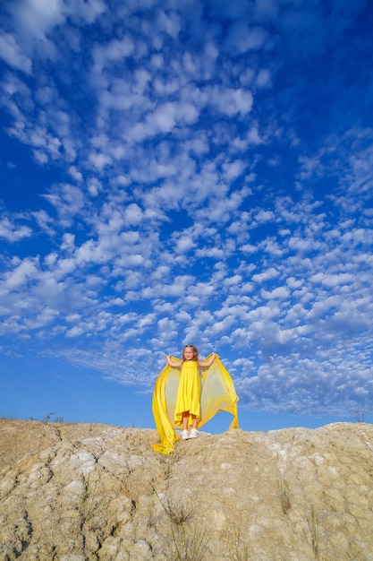 Ein blondes Mädchen von 7-8 Jahren in einem leuchtend gelben Kleid vor blauem Himmel.