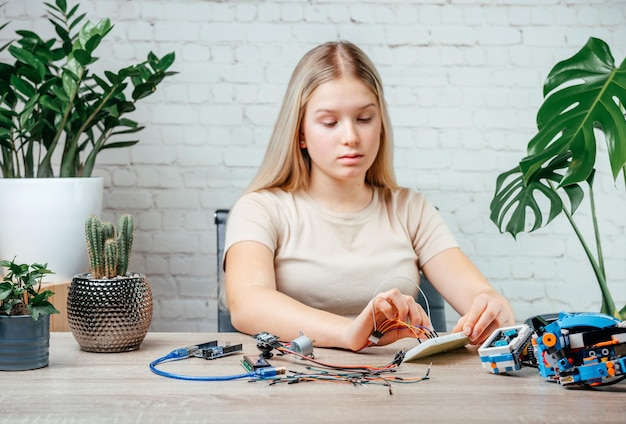 Ein blondes Teenager-Mädchen, das Kabel an Sensorchips anschließt, während sie Arduino-Codierung und Robotik lernt