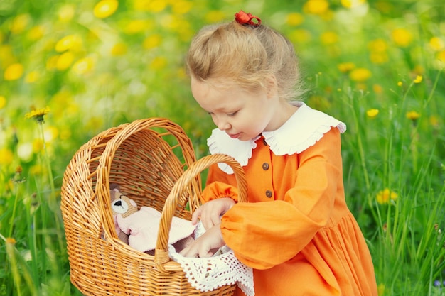 Ein blondes Vorschulmädchen in einem Kranz aus Eberesche und mit Spielzeug geht an einem Sommermorgen im Park spazieren