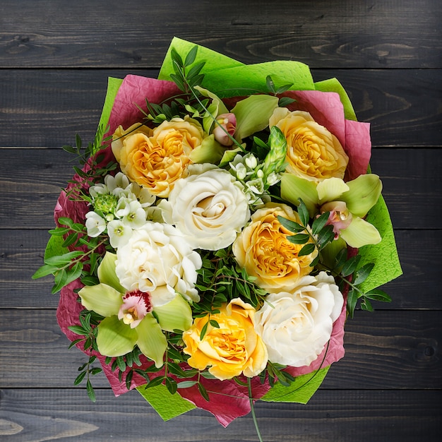 Ein Blumenstrauß auf einem dunklen hölzernen Hintergrund. Blumenstrauß mit Rosen