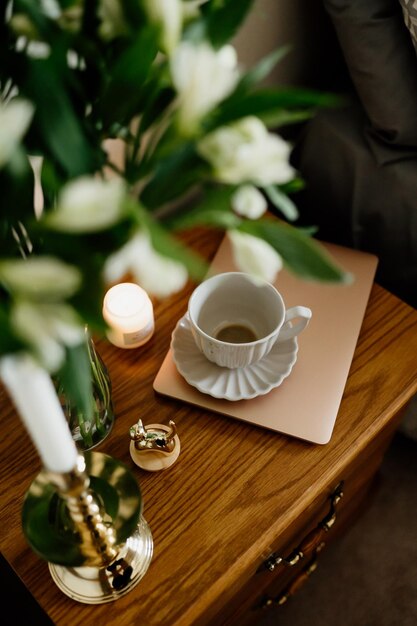 Ein Blumenstrauß, eine Tasse Tee oder Kaffee mit Milch und Süßigkeiten auf dem Tisch.