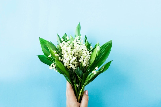 Ein Blumenstrauß von Maiglöckchen in den weiblichen Händen auf einem blauen Hintergrund