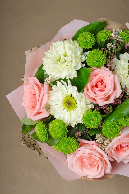 Ein Blumenstrauß von Rosen im Kraftpapier auf einem beige Hintergrund.