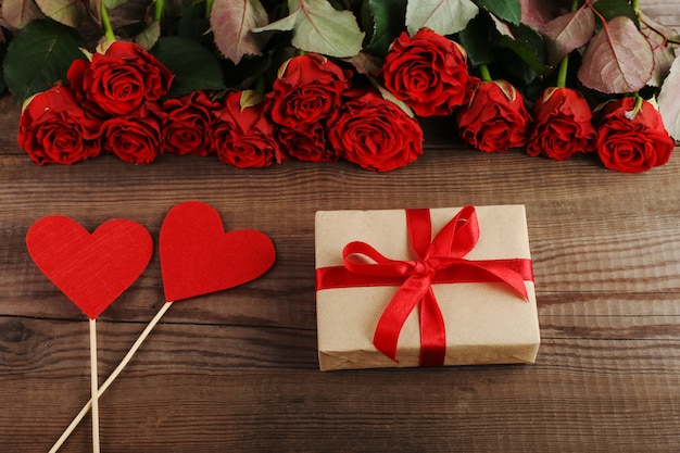 Ein Blumenstrauß von roten Rosen, von Geschenk und von Herzen auf Holztisch