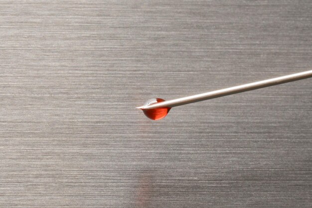 Ein Blutstropfen an der Nadelspitze auf der Metalloberfläche