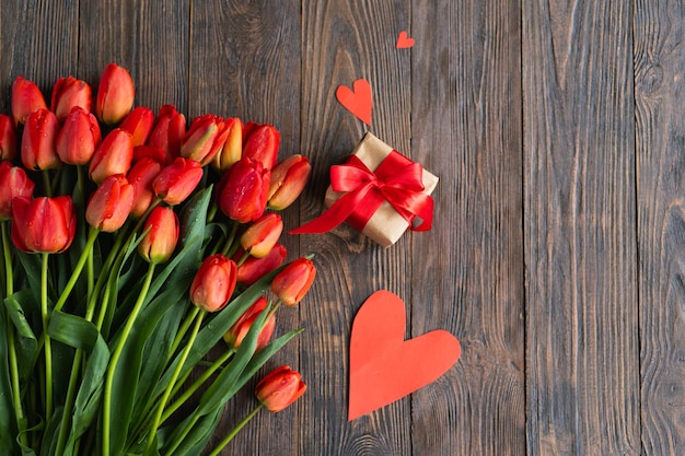 ein Bouquet aus Tulpen mit Geschenkkiste und roten Herzen auf Holzgrund.