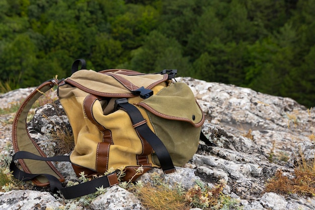 Ein braungrüner Rucksack liegt auf einem großen grauen Stein auf einem Felsen vor dem Hintergrund grüner Berge