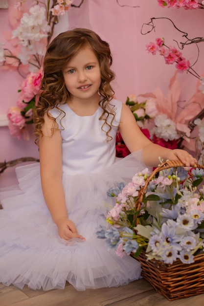Ein braunhaariges Mädchen in einem weißen Kleid steht im Studio vor einem Blumenhintergrund