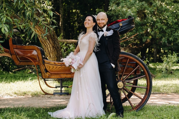 Ein Brautpaar steht im Retro-Stil in der Nähe der Kutsche in der Natur