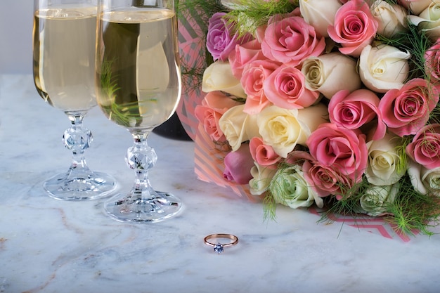 Ein Brautstrauß aus zarten Rosen und Ring mit einem Diamanten zwei Gläser Champagner für die Hochzeit Valentinstag