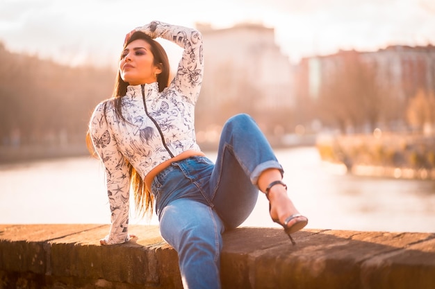 Ein brünettes lateinisches mädchen in der stadt bei sonnenuntergang am fluss mit der sonne im hintergrund