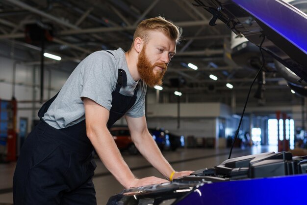 Ein brutaler bärtiger Mann in Uniform arbeitet an einer Autowerkstatt und überprüft das Auto in einem sauberen, modernen Raum