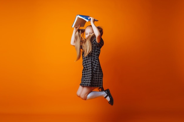 Ein Buchdach über dem Kopf Ein kleines Mädchen hält ein Lehrbuch auf dem Kopf Ein kleines Mädchen mit einem Buch auf einem orangefarbenen Hintergrund