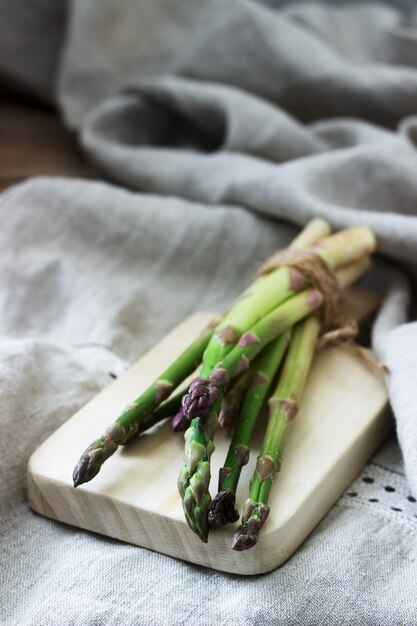 Ein Bündel frischer Spargel, mit Schnur zusammengebunden, gegen eine Leinentischdecke. Rustikaler Stil.