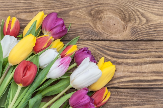 Ein Bündel mehrfarbige Tulpen in einer Ecke auf einem Hintergrund des hellen Holzes.