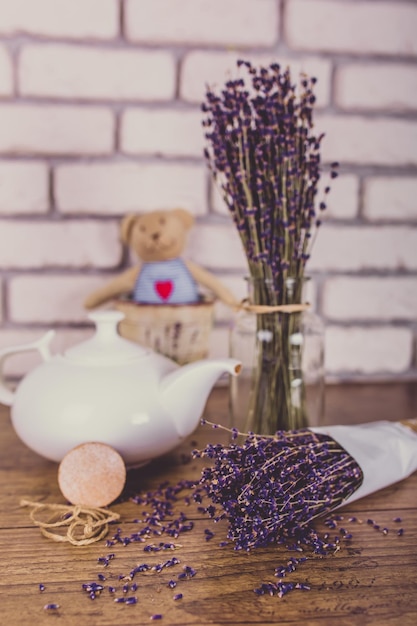 Ein Bündel trocken geschnittener Lavendel und eine Teekanne auf einem Holztisch mit weißem Backsteinhintergrund