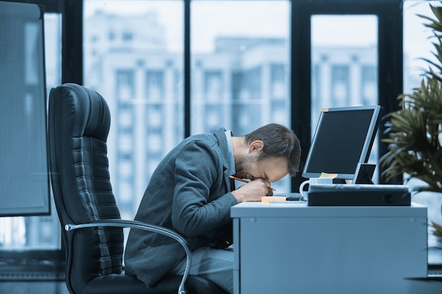 Ein Büroangestellter lacht über seinen Schreibtisch. Auf dem Tisch steht ein Computer und eine Tasse heißes Getränk