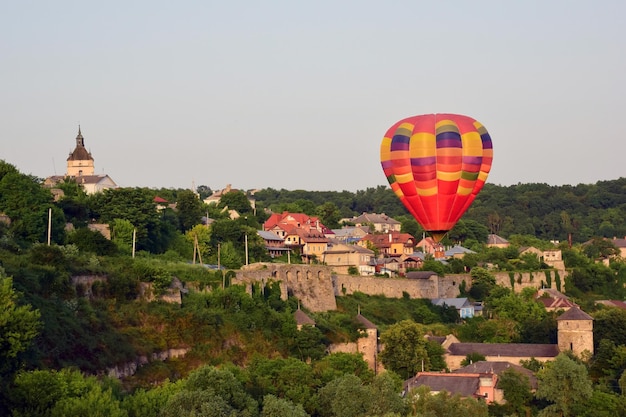 Ein bunter aufblasbarer Ballon mit einer Gondel fliegt über die antike Stadt und den grünen Wald