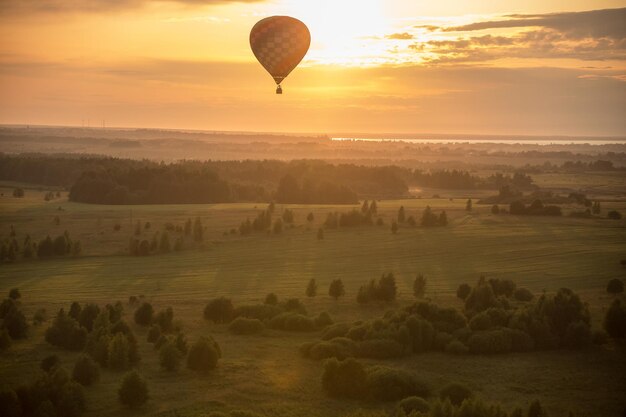 Ein bunter Heißluftballon, der über den leuchtend gelben Sonnenuntergang des Feldes fliegt