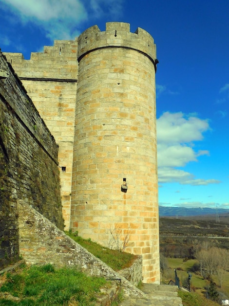 Ein Burgturm mit einer Steinmauer und einer grünen Wiese im Hintergrund.