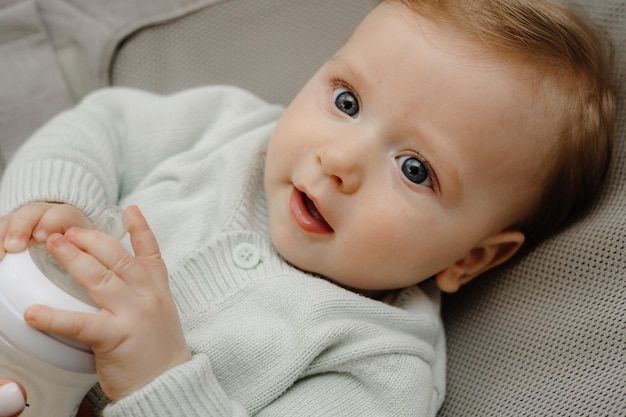 Ein charmantes blauäugiges Baby von 5 Monaten liegt im Bett und trinkt Milch aus einem Flaschenbaby mit einer Flasche