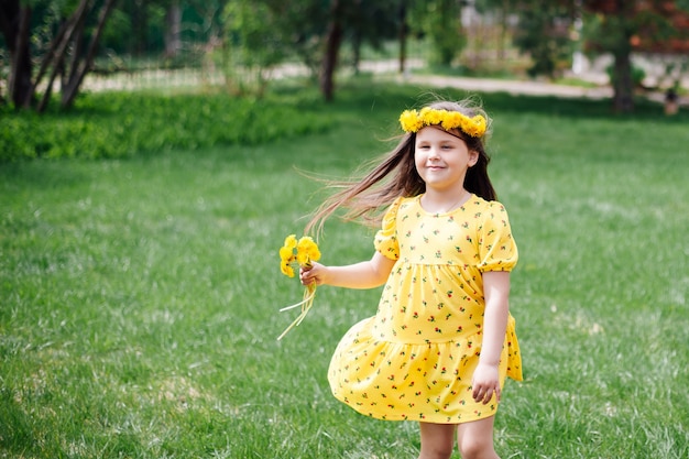 Ein charmantes glückliches Mädchen in einem Kleid, das im Wind fliegt, läuft auf dem grünen Gras und mit Löwenzahn in h...