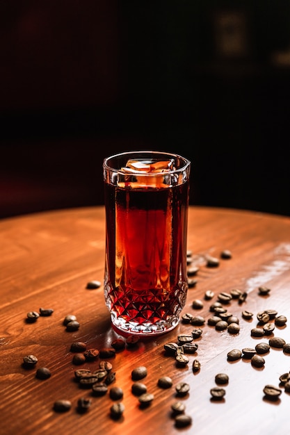 Ein Cocktail in einem Collins Highball-Glas mit einem Eisspeer, Kaffeebohnen herum, auf einem Holztisch an der Bar.