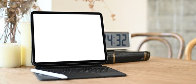 Ein Computertablett mit einem weißen leeren Bildschirm stellt einen Holztisch auf, der von verschiedenen Geräten umgeben ist.