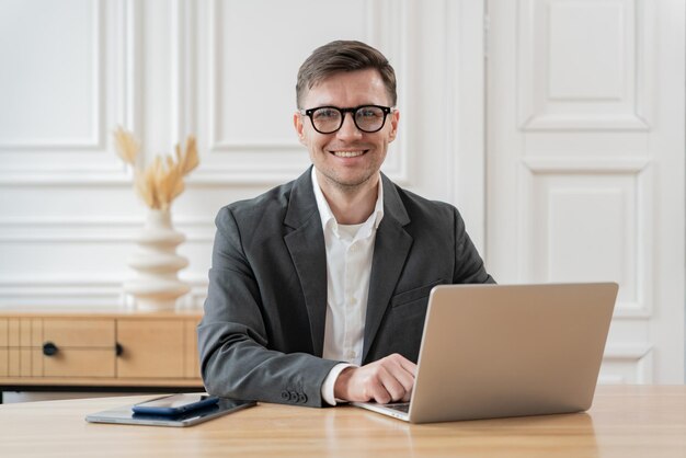 Ein Content-Geschäftsmann in einem grauen Anzug arbeitet an seinem Laptop mit einem Smartphone und Tablet auf dem Schreibtisch