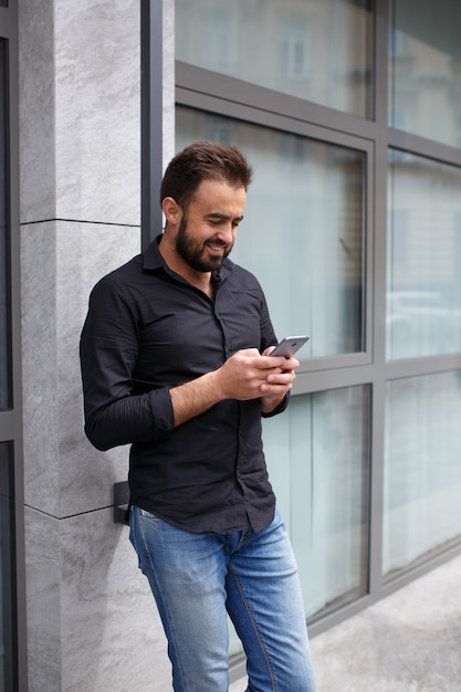 Ein cooler junger Mann benutzt ein Smartphone. Hipster mit Bart schreibt eine Nachricht in sein Handy. Speicherplatz kopieren.