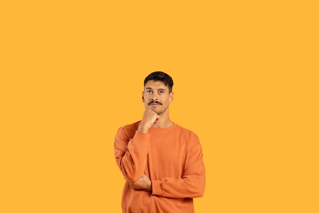 Ein denkender Typ mit der Hand auf dem Kinn auf der Orange