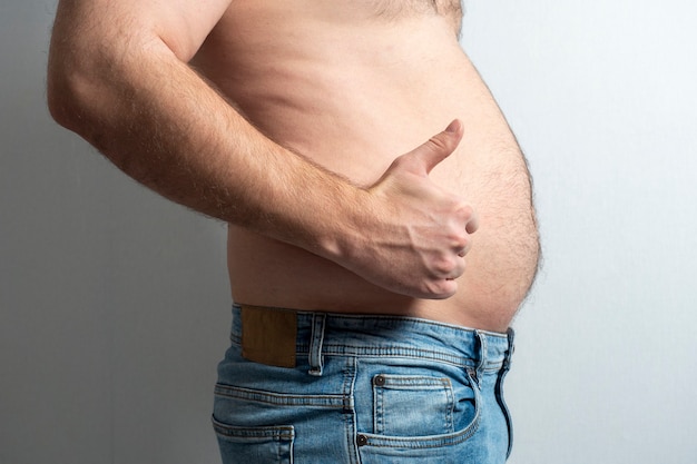 Ein dicker Mann in Jeans mit nacktem Bauch und erhobenem Finger. Das Konzept der Körperpositivität. Selbstakzeptanz