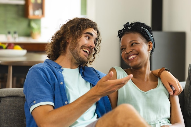 Ein diverses Paar, ein junger kaukasischer Mann und eine afroamerikanische Frau, teilen sich einen freudigen Moment auf einer Couch.