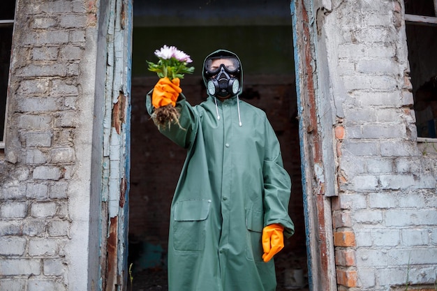 Ein Dosimetrist-Wissenschaftler in Schutzkleidung und Gasmaske untersucht die Gefahrenzone Closeup Blume in Händen