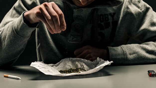 Ein Drogenabhängiger macht eine Zigarette mit Marihuana Das Konzept von Drogenmissbrauch und -verkehr