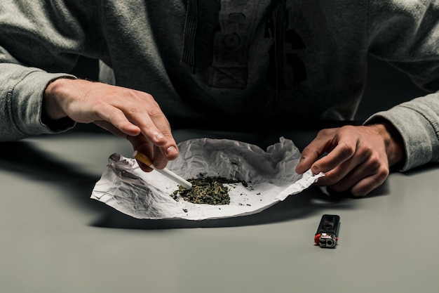 Ein Drogenabhängiger macht eine Zigarette mit Marihuana Das Konzept von Drogenmissbrauch und -verkehr