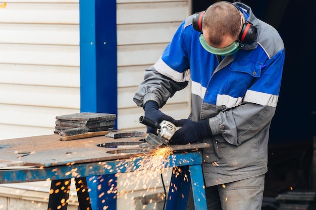 Ein echter Arbeiter in Arbeitskleidung schleift Metalloberflächen und Funken fliegen bei der Arbeit